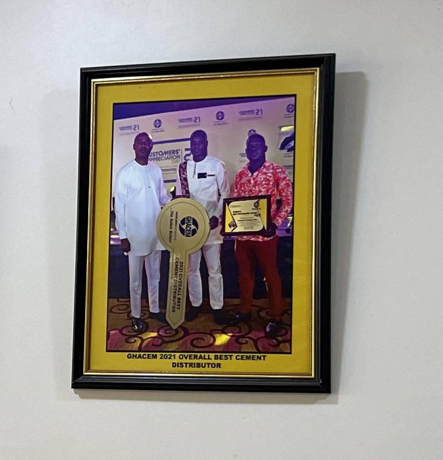 Framed photo captioned GHACEM 2021 OVERALL BEST CEMENT DISTRIBUTOR: three men at Ghacem's Customers' Appreciation Day 2021, one holding a giant ceremonial key reading 2021 Overall Best Cement Distributor, another holding an award plaque