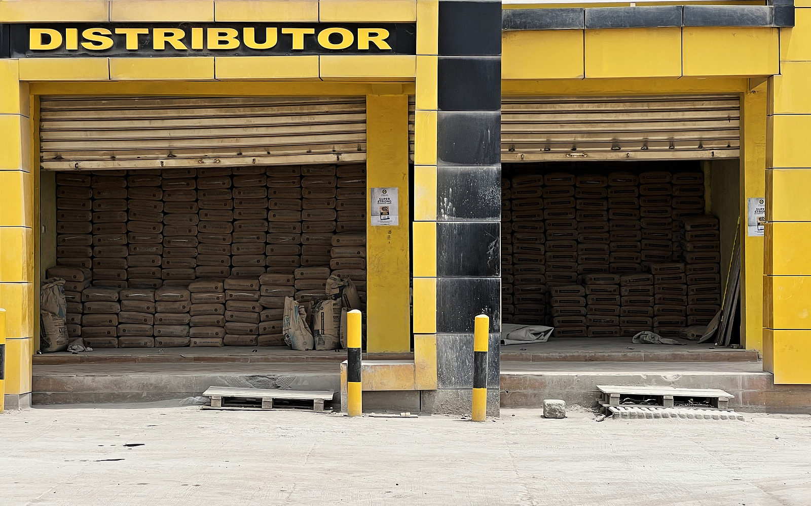 Two open bays stacked high with bags of Ghacem cement under a Distributor sign