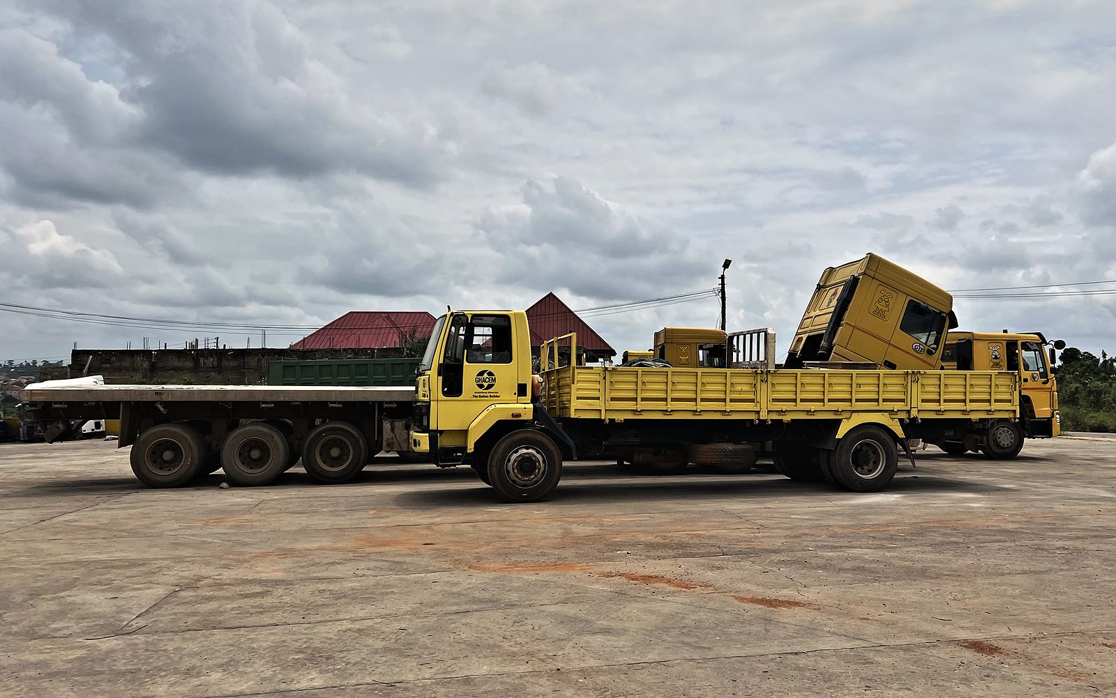 Clemonic’s yellow trucks lined up in the yard, including a flatbed and a cargo truck with the Ghacem logo on its cab