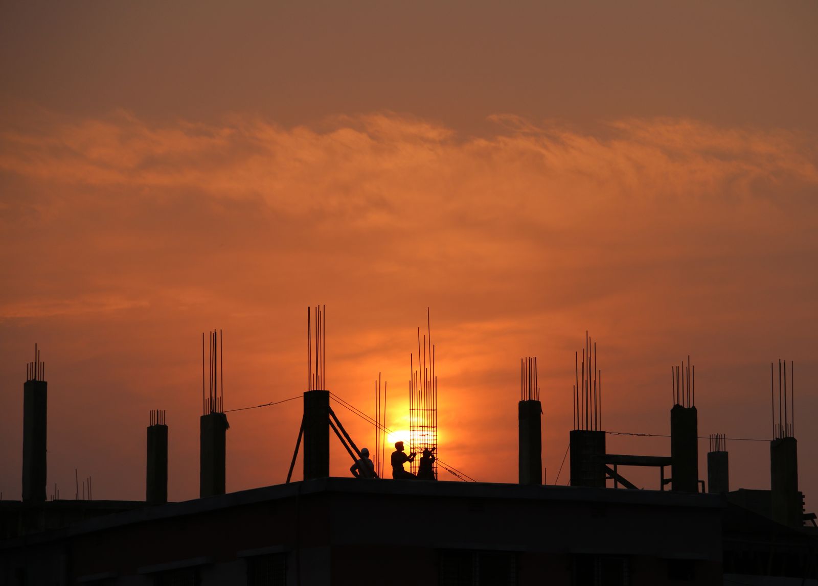 Construction site at golden hour — reinforced concrete columns rising against the evening sky
